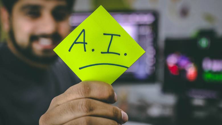 Smiling man holding a post-it with the acronym artificial intelligence (AI)
